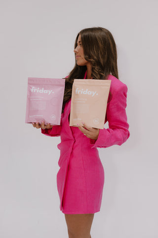 Woman in a bright pink blazer holding two Friday Wellness supplement bags
